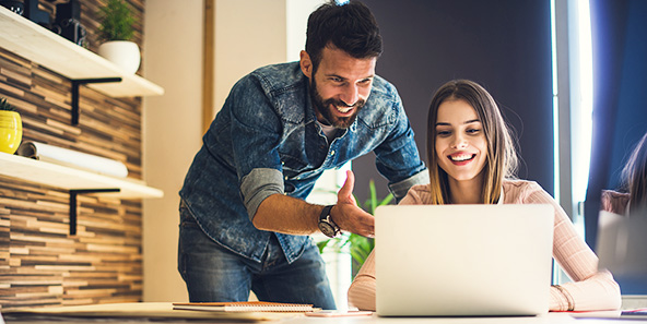 Husband And Wife Smile At Computer Screen While Learning More About Health Insurance Plans